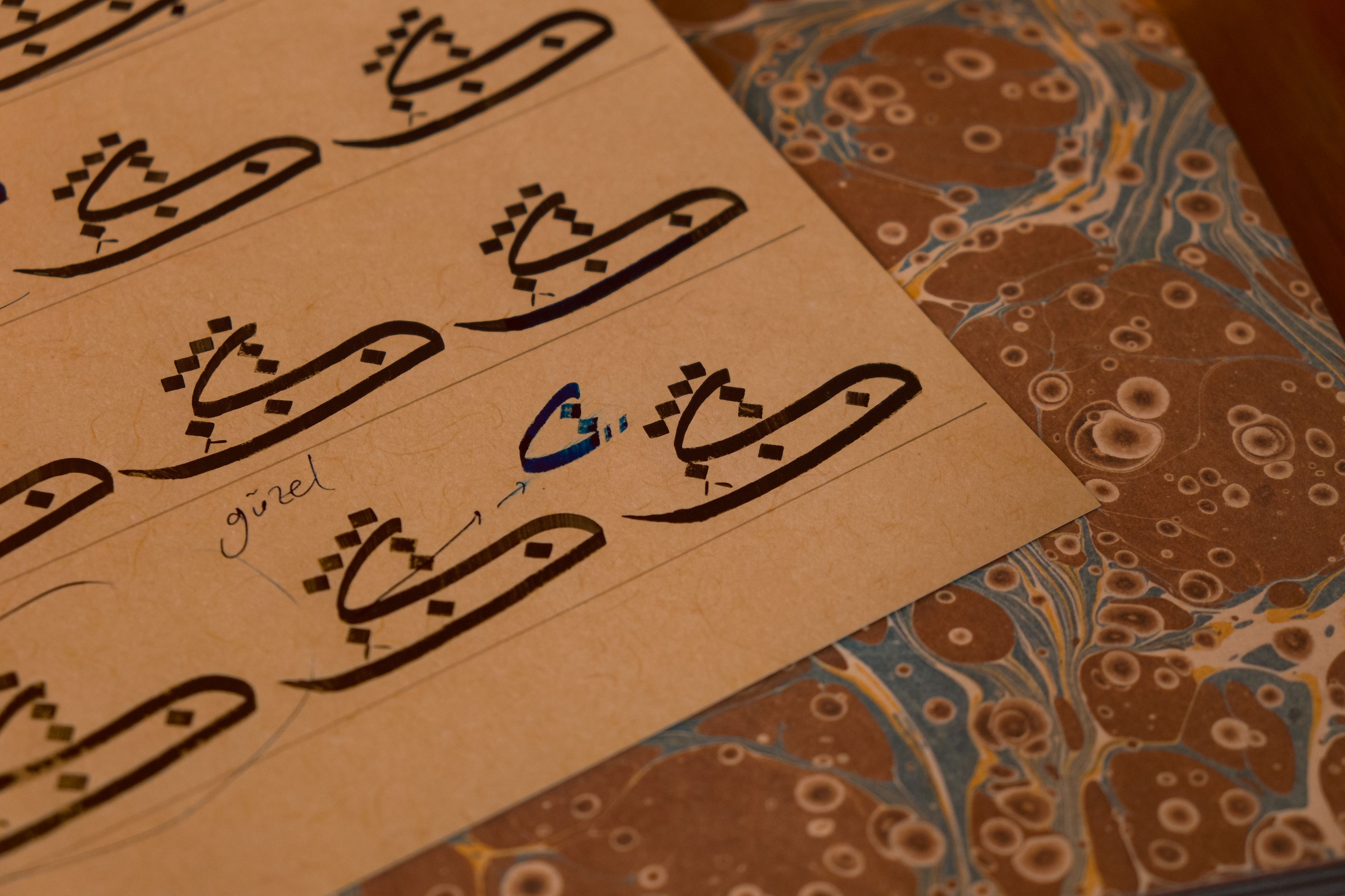 A close-up of Arabic calligraphy drawn on textured paper with marbled patterns.
