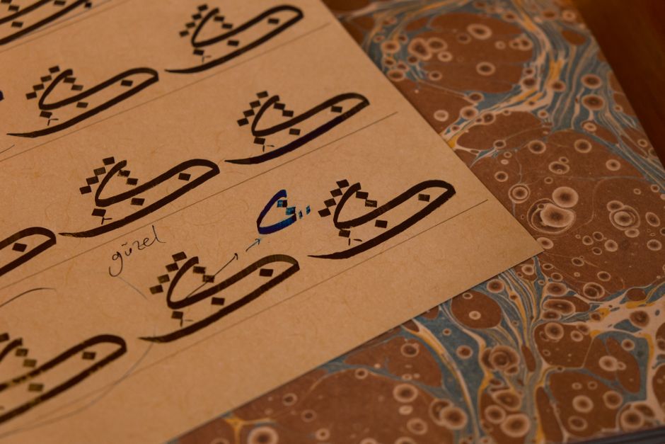 A close-up of Arabic calligraphy drawn on textured paper with marbled patterns.