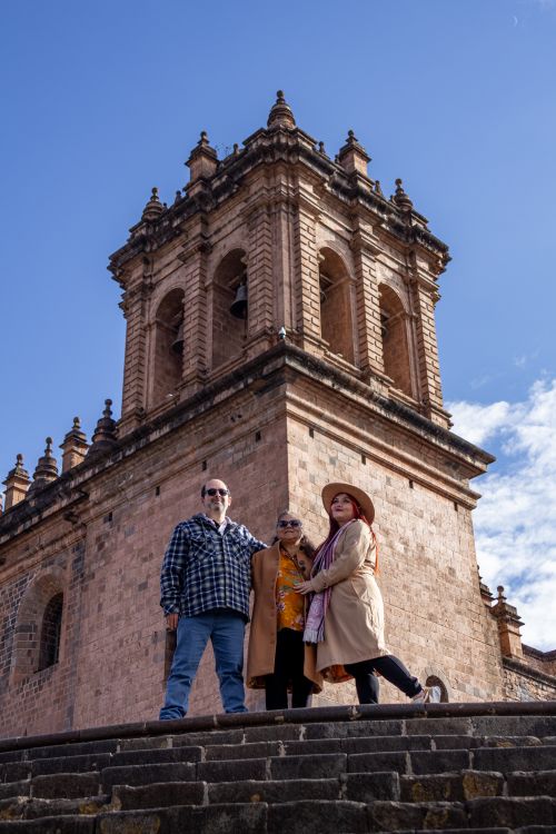 Free Three adults standing in front of a historic tower in Cusco, Peru, enjoying a sunny day. Stock Photo