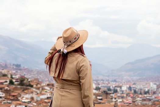 A woman in a hat gazes over the rooftops of Cusco, with the Andes mountains in the background.