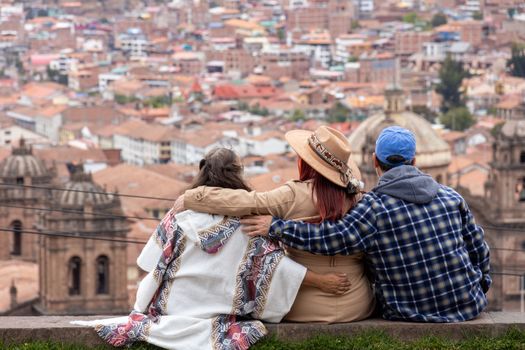 Three people embracing while enjoying a panoramic view of Cusco city with historic architecture.