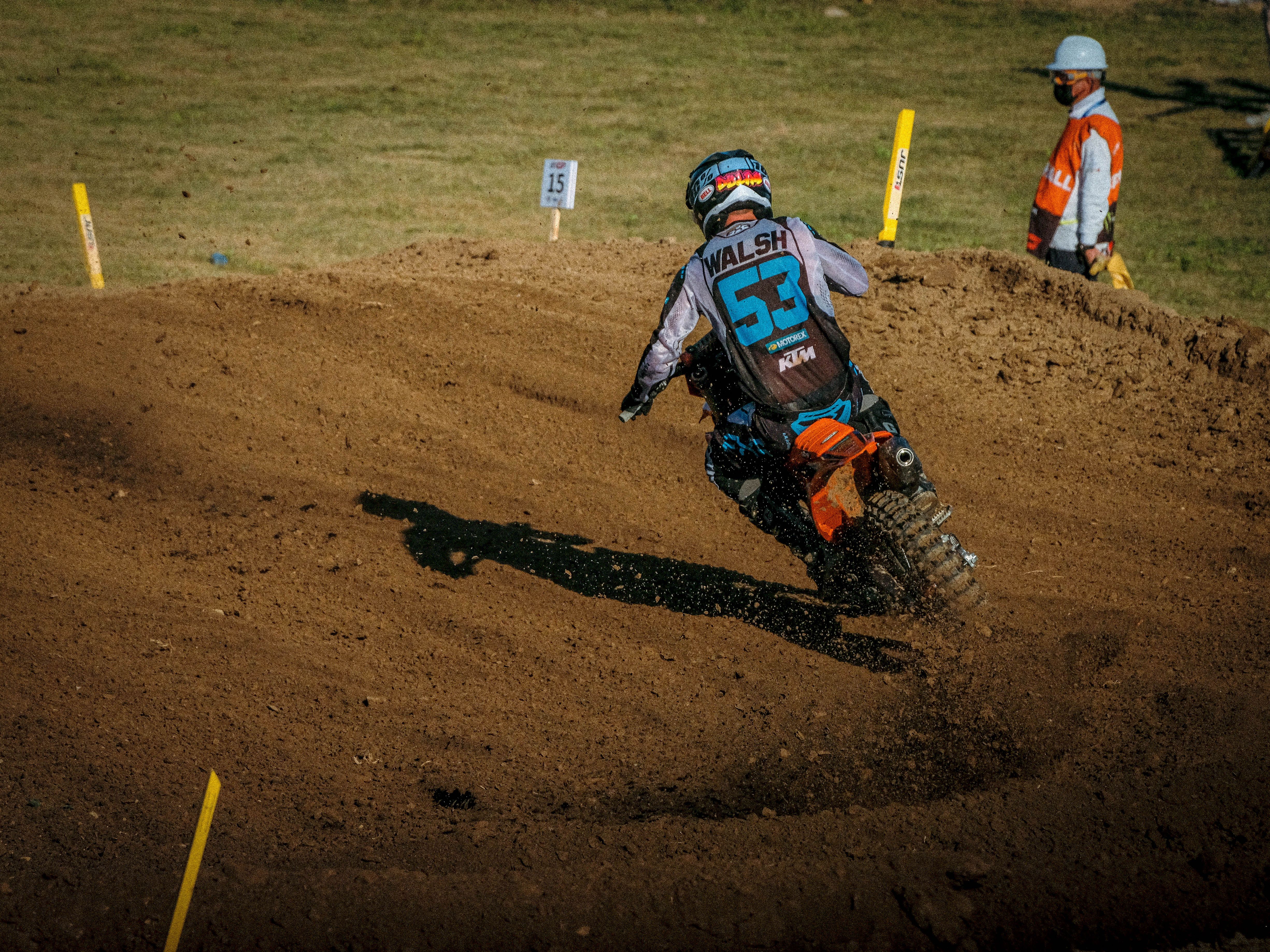 Dirt bike racer navigating a curve on a motocross track under bright daylight.