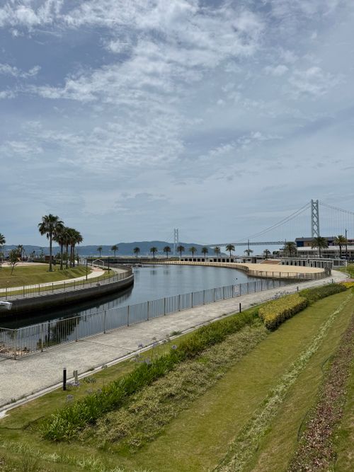 Free A picturesque scene in Kobe, Japan, featuring the iconic Akashi Kaikyō Bridge over a calm waterway. Stock Photo