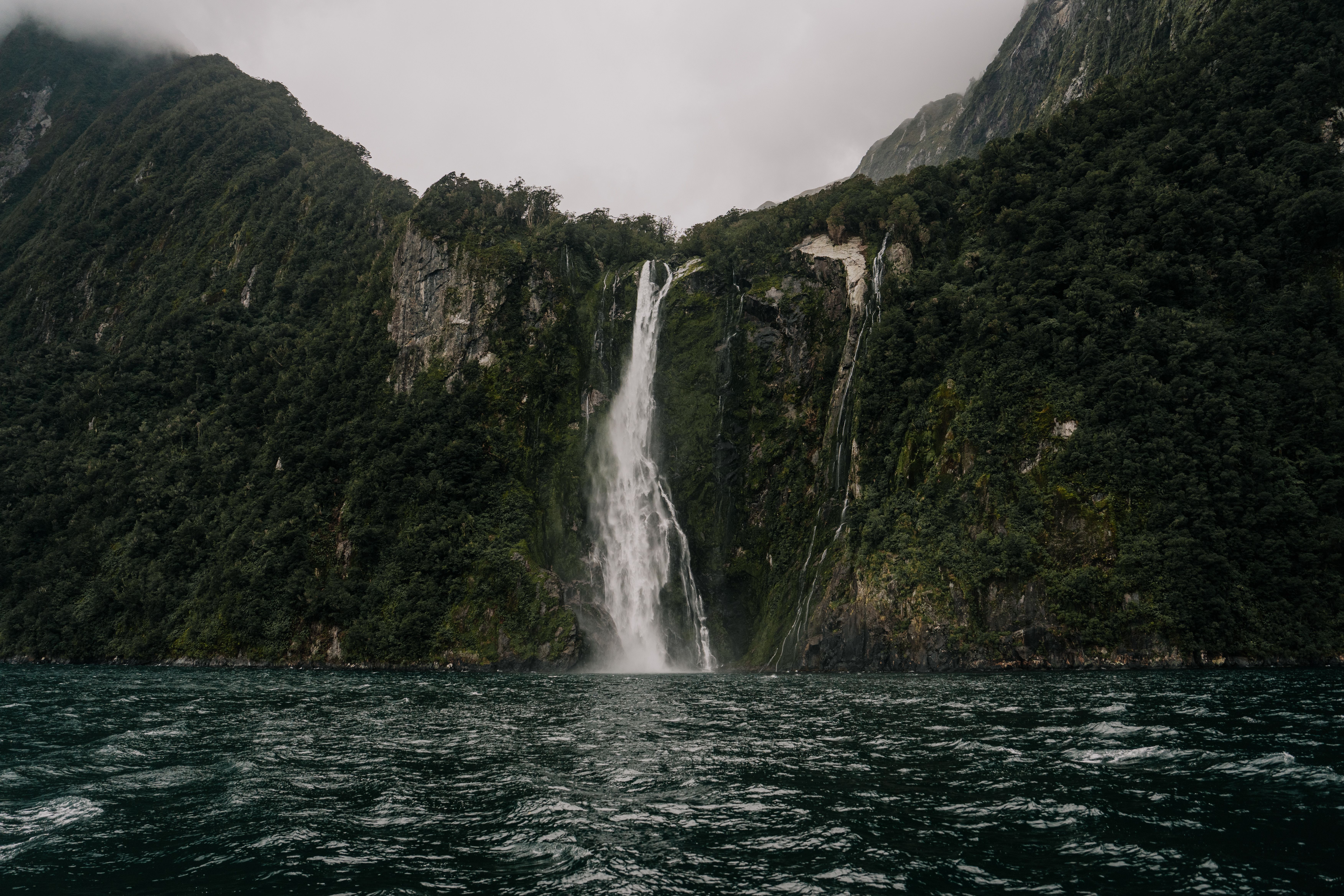 Stunning view of a waterfall cascading in Milford Sound, surrounded by lush greenery and mist.