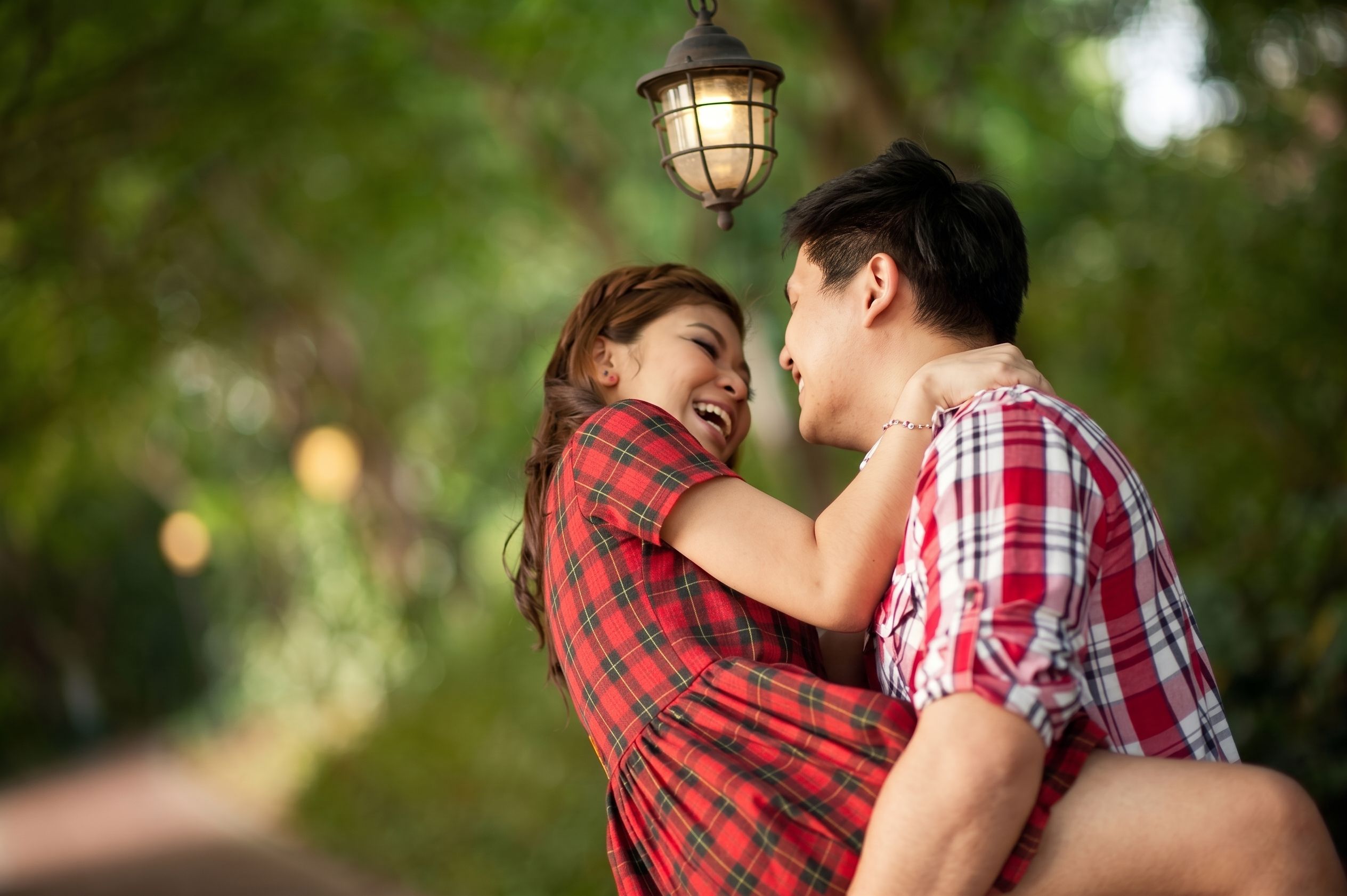 Cheerful couple in love embracing outdoors under a lamp in lush Singapore park.