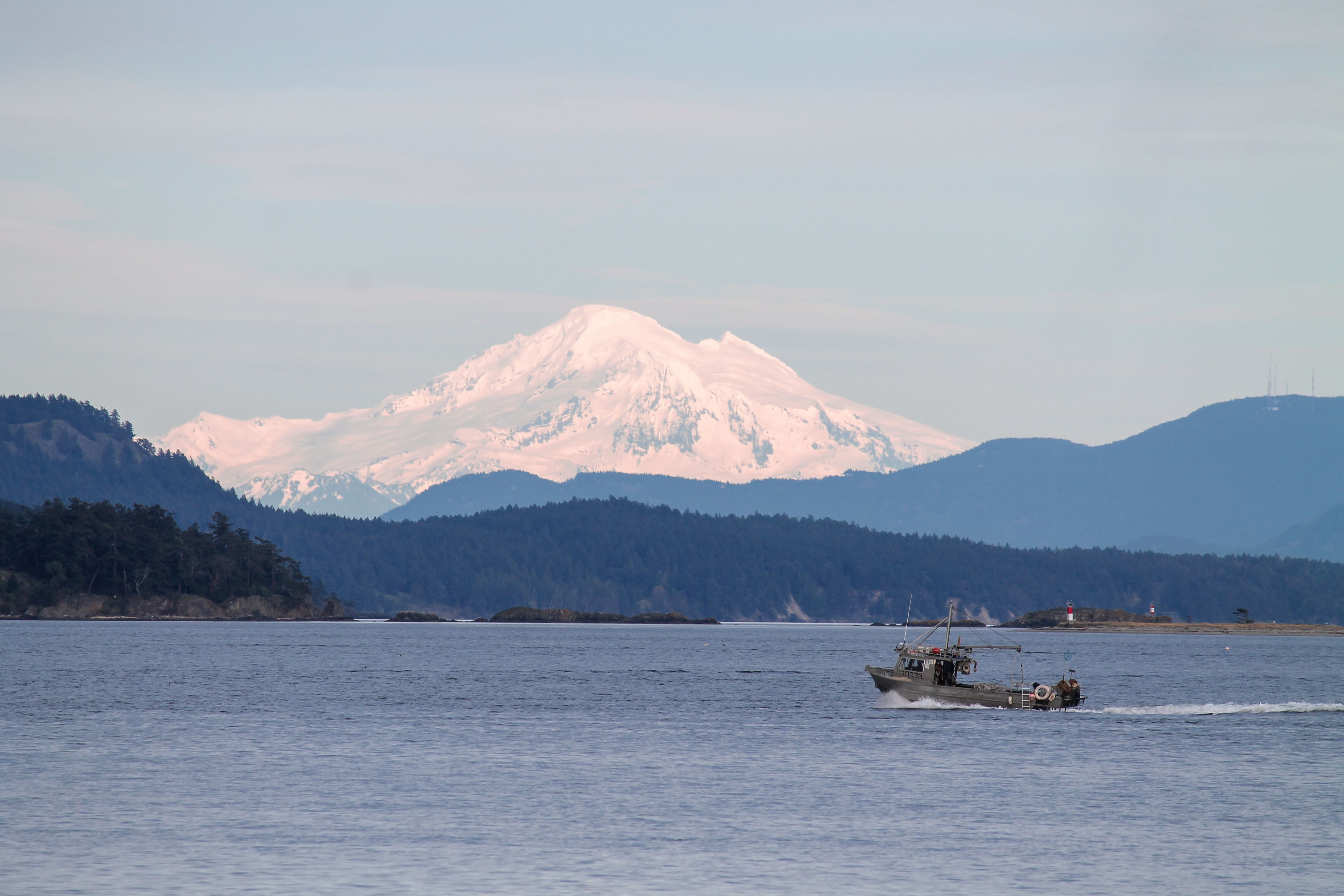 A serene coastal scene near Victoria, BC, with a boat on calm waters and snow-capped mountains in the background.