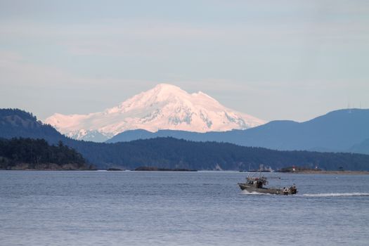 A serene coastal scene near Victoria, BC, with a boat on calm waters and snow-capped mountains in the background.