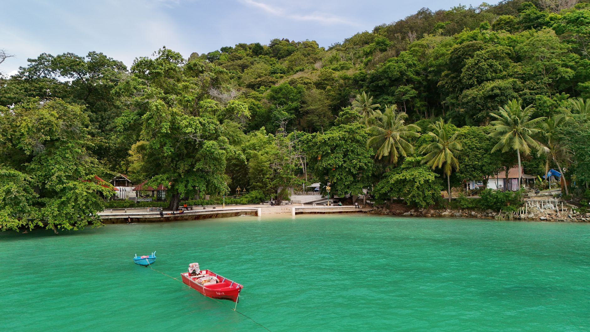 Scenic view of turquoise waters and lush greenery on a tropical beach in Thailand with red and blue boats.