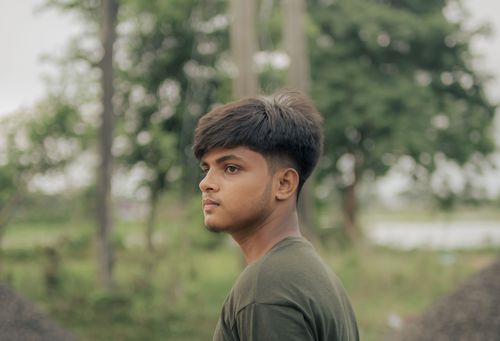 Free A serene portrait of a young man standing outdoors, surrounded by lush green trees and natural beauty. Stock Photo