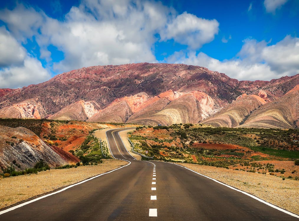 Concrete Road Near Brown Mountain Under Blue Sky