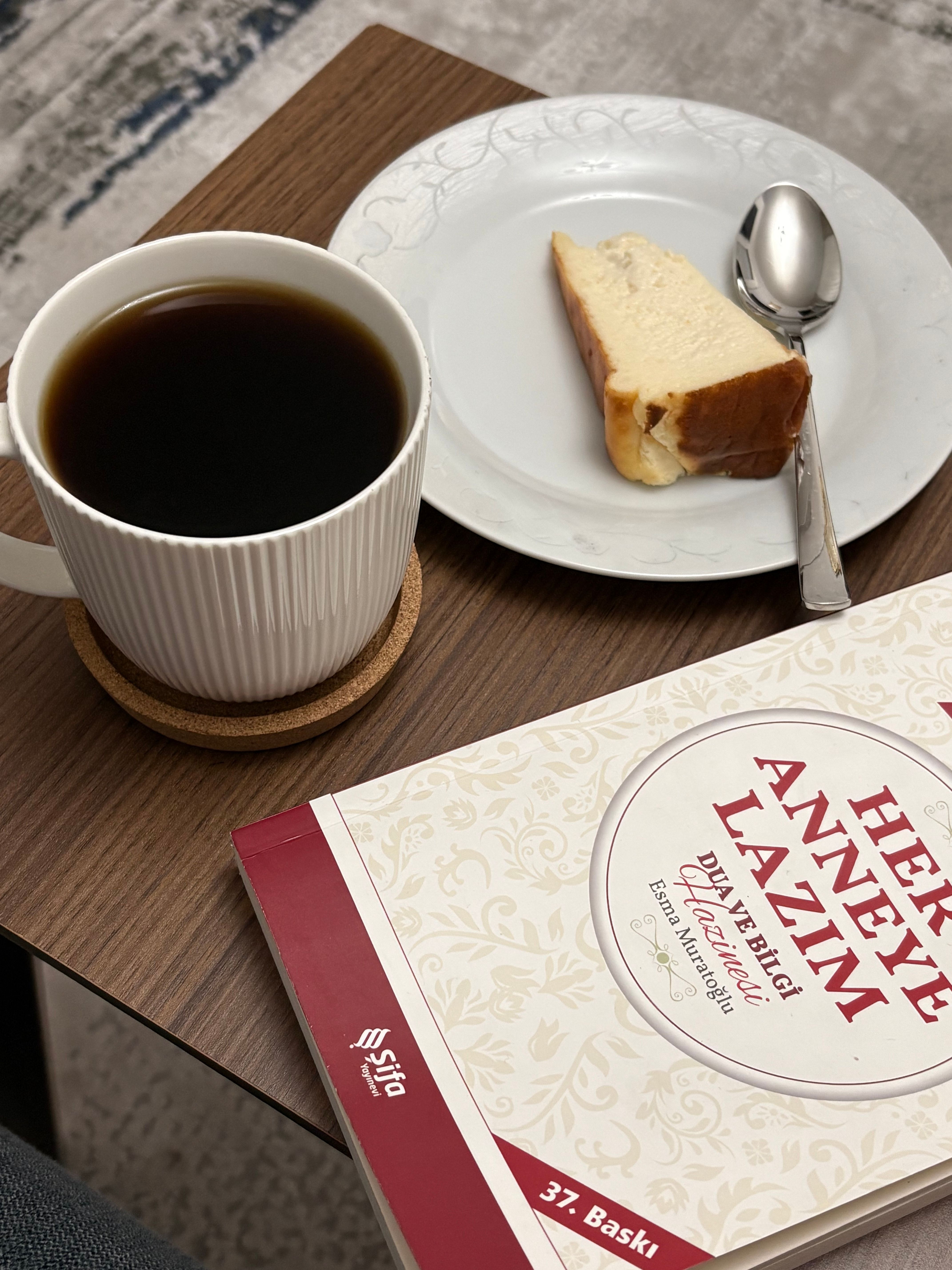 A cozy indoor setting featuring a cup of coffee, a slice of cake, and a book on a wooden table.
