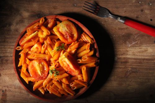 Free Appetizing penne pasta with sliced tomatoes on a rustic wooden table. Stock Photo