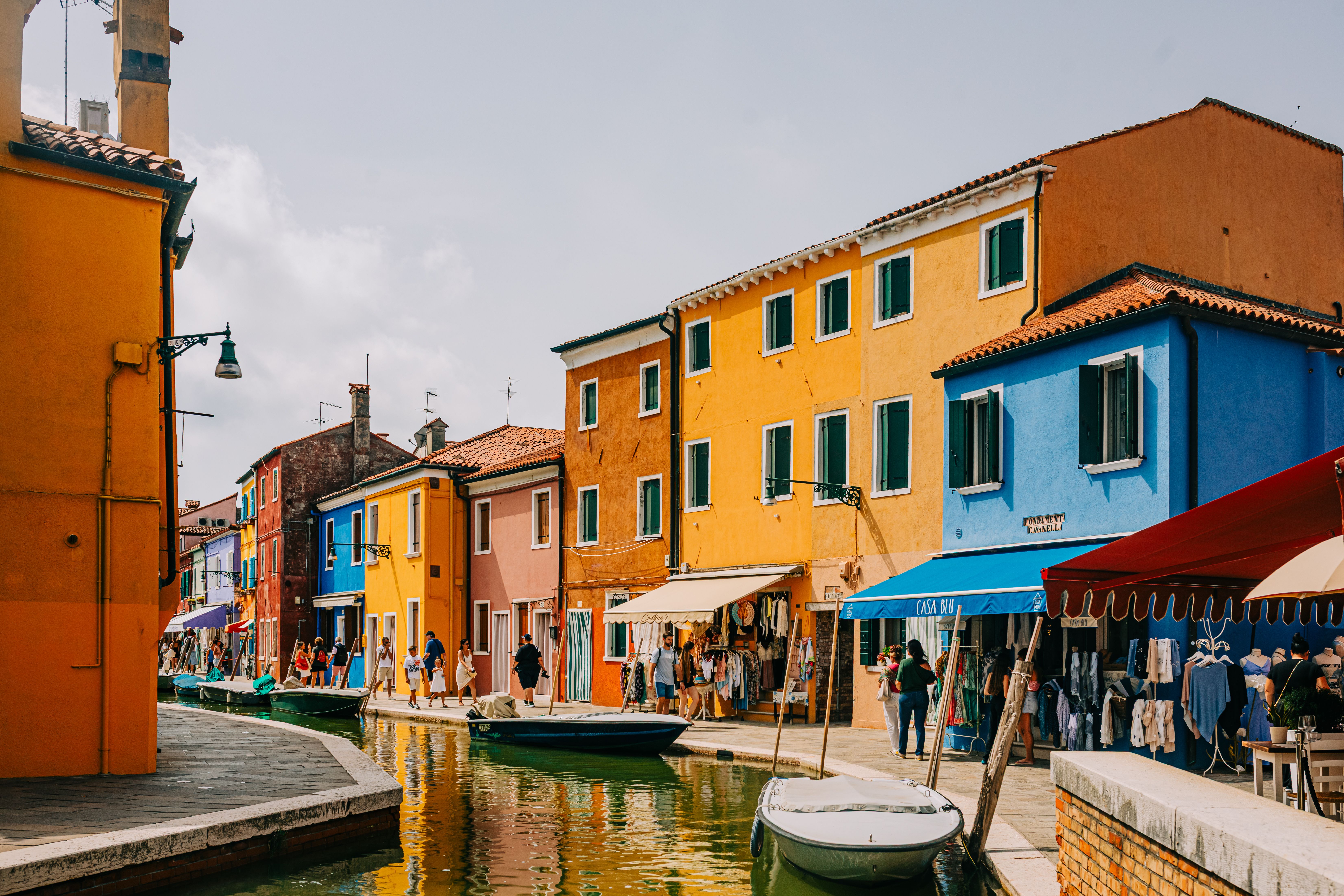 Fotomural Vista panorámica de coloridas casas a lo largo de un canal en Burano, Italia, llena de gente.