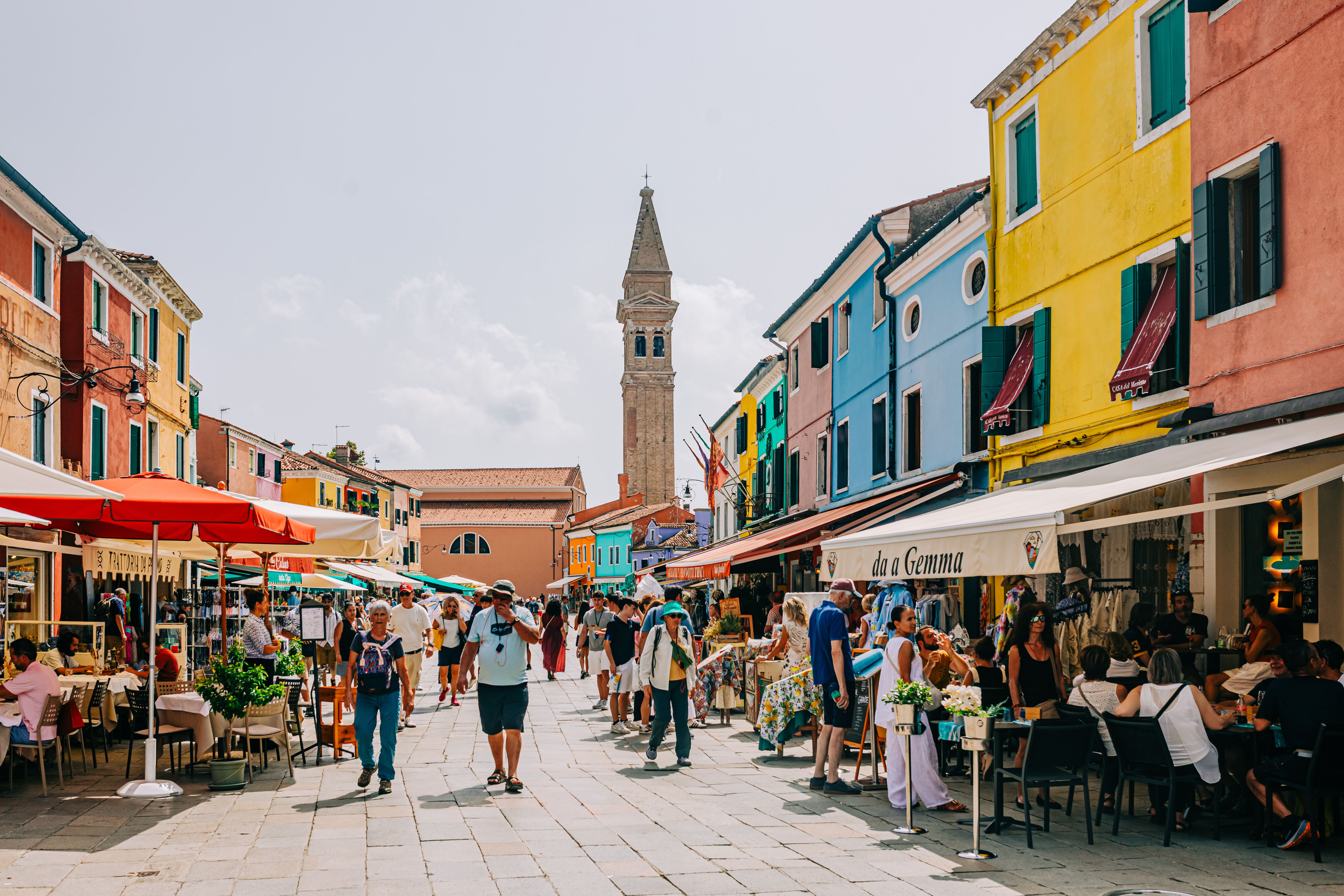 Vibrant street life in Burano, Italy with colorful buildings and people enjoying cafes.