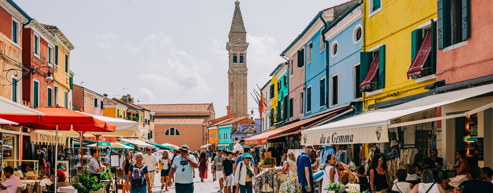 Vibrant street life in Burano, Italy with colorful buildings and people enjoying cafes.