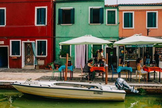Vibrant outdoor cafe along a canal in Burano, Italy, with colorful houses.
