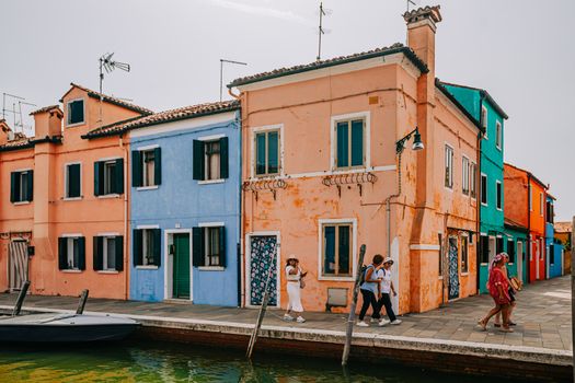 Vibrant houses and pedestrians on a canal street in Burano, Venice.