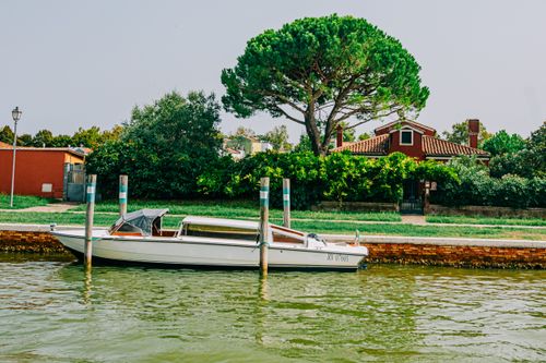 Free A serene canal with a docked boat and a house surrounded by lush greenery on a sunny day. Stock Photo