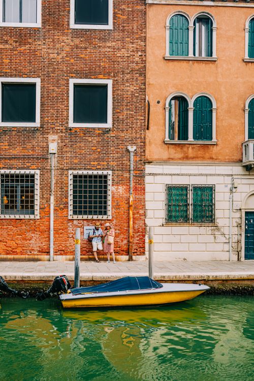 Free Children enjoy a sunny day along a vibrant Venetian canal with a striking yellow boat. Stock Photo