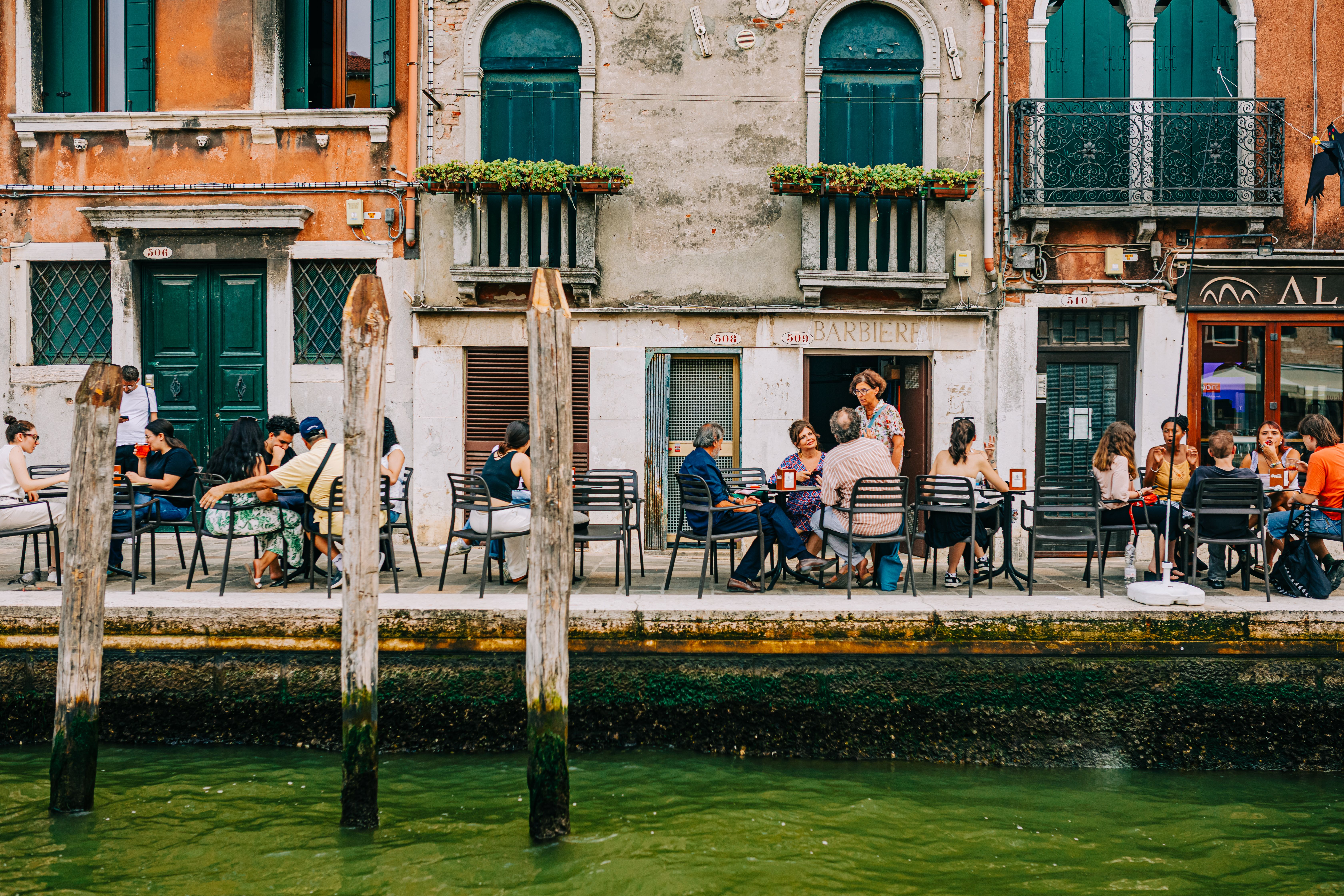 A vibrant scene capturing people dining at an outdoor cafe by a canal in Venice, Italy.