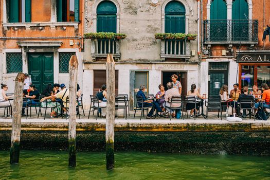 A vibrant scene capturing people dining at an outdoor cafe by a canal in Venice, Italy. - Fotografer Sidoarjo