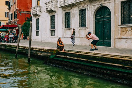 Free A tourist captures a photo of a woman by the canal in Venice, Italy on a sunny day. Stock Photo