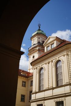 Historic building with a tower in Praga, Cechia, framed by an archway under a blue sky.