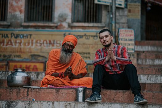 A local and a traveler sitting together at the ghats of Varanasi, India, sharing a cultural moment.