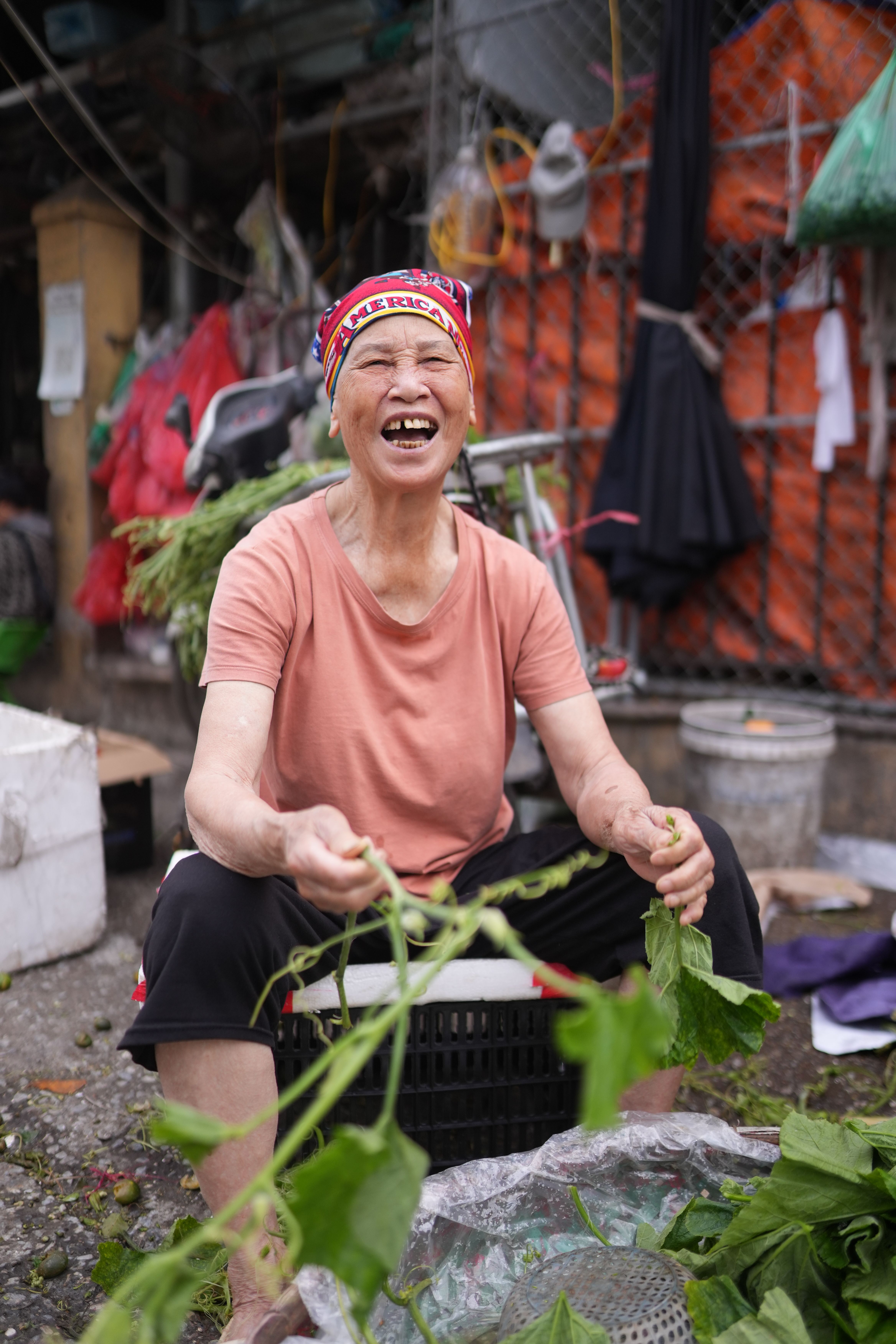 Smiling elderly woman selling fresh greens at a vibrant Hanoi market, showcasing local culture.