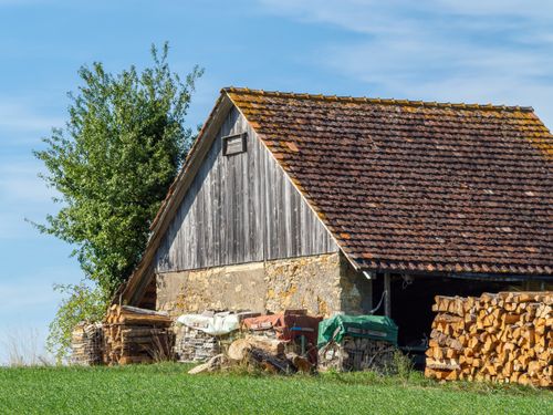 Free Charming rustic barn with stacked firewood under a clear blue sky. Stock Photo
