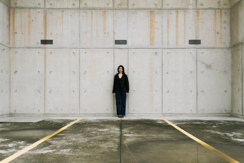 Free Person stands alone against a concrete wall in an urban parking space. Stock Photo