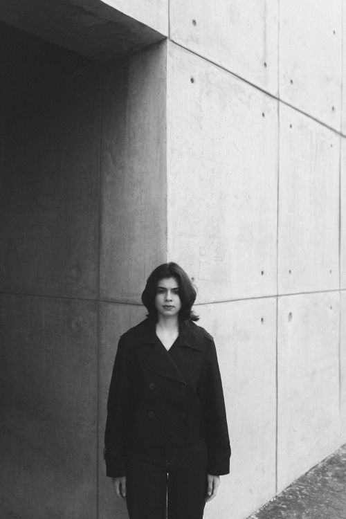 Free A black and white portrait of a young adult standing near a modern concrete wall. Stock Photo