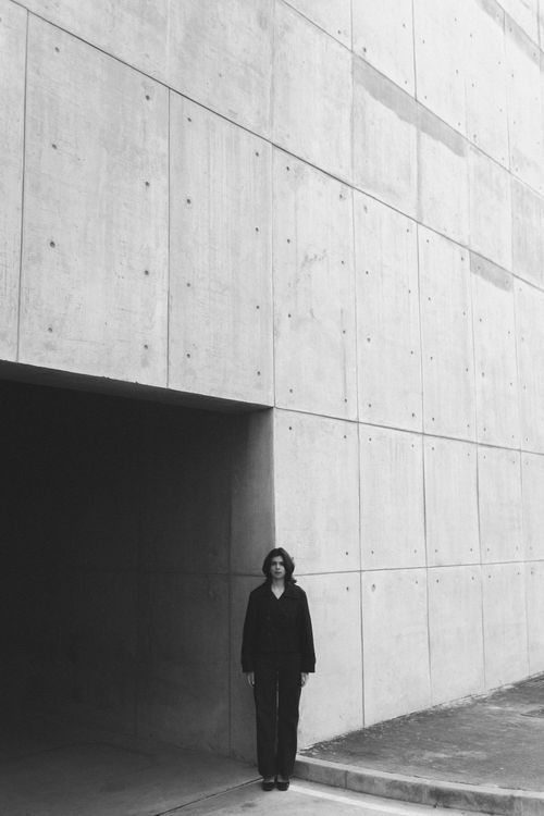 Free A solitary figure stands against a minimalist concrete wall, captured in black and white. Stock Photo