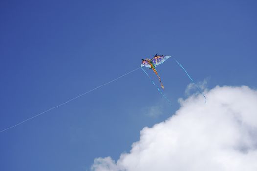 Vibrant kite soaring in a clear blue sky with fluffy clouds below.