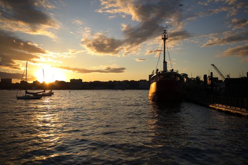 Free Vibrant sunset casting dramatic silhouettes on boats over a serene river. Stock Photo