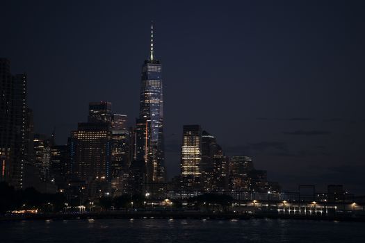 Night view of One World Trade Center in New York City with illuminated skyscrapers.