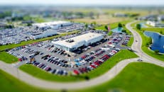 从高角度鸟瞰，一家热闹的汽车经销店周围停满了汽车，点缀在绿色景观中