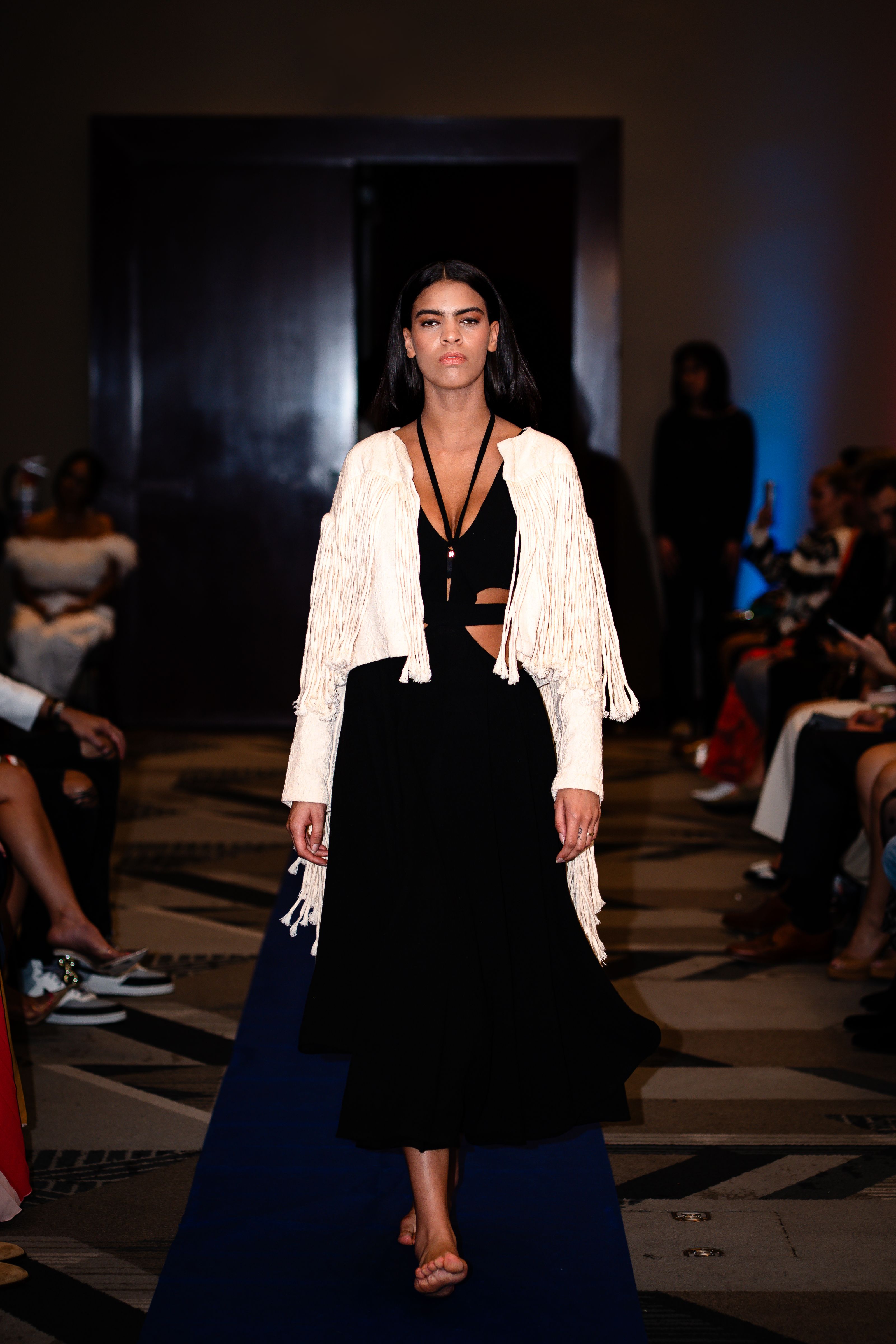 Modelo elegante na passarela, vestindo um sofisticado vestido preto com jaqueta branca durante um desfile de moda.