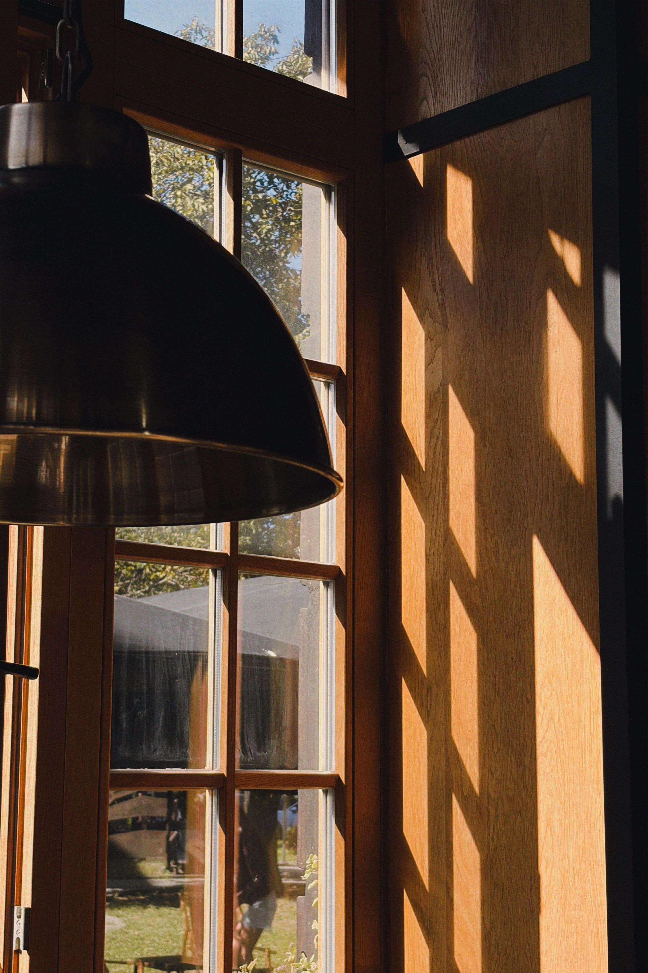 Fotomural La cálida luz del sol proyecta sombras a través de una ventana de madera con una lámpara colgante.