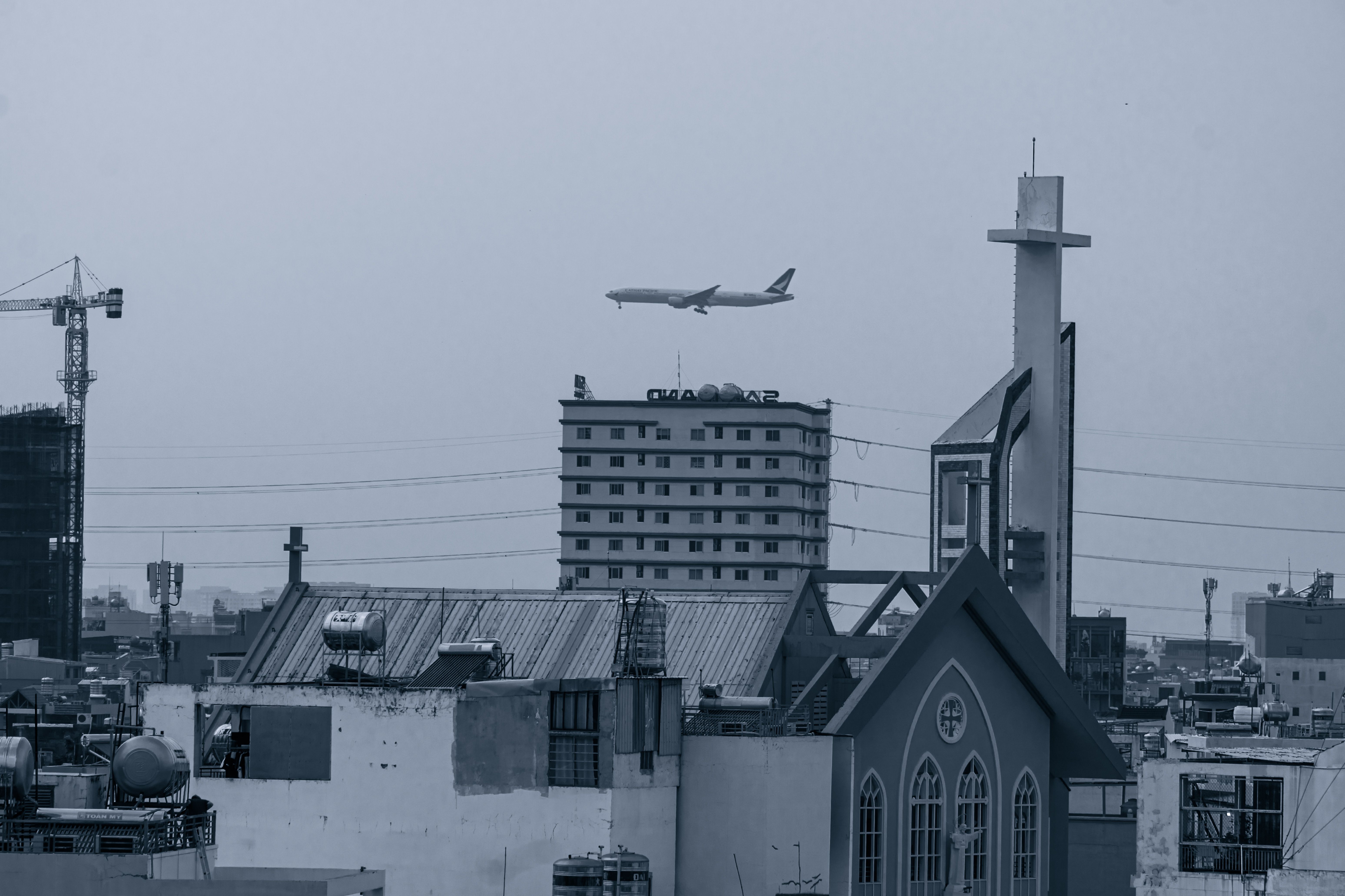 Urban skyline featuring architecture, a flying airplane, and construction cranes in the background.