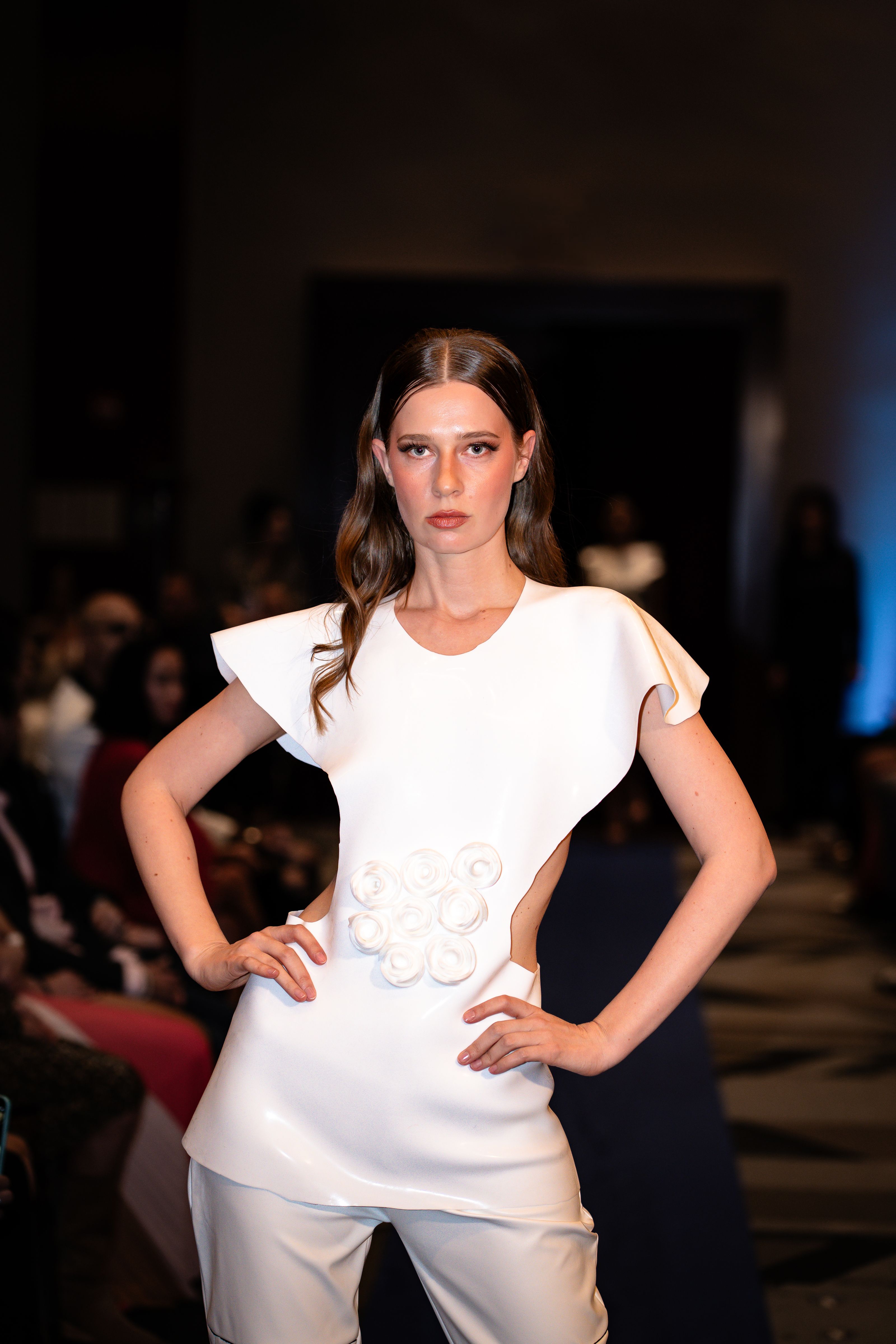 Elegante modelo posando na passarela com um sofisticado vestido branco durante um desfile de moda em ambiente fechado.