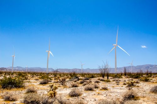 Free Wind turbines stand tall in a vast desert landscape under a clear blue sky. Stock Photo
