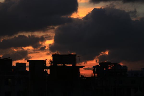 A silhueta da cidade recortada contra um pôr do sol vibrante, destacando nuvens dramáticas.