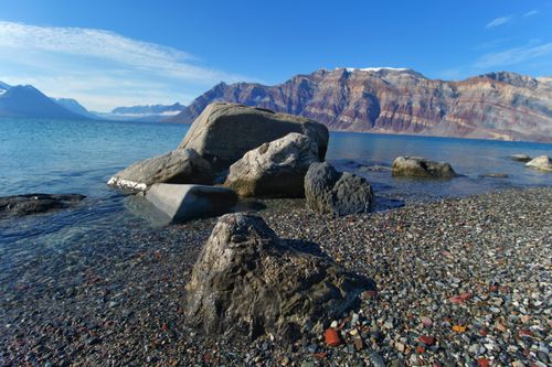 Free Explore a tranquil rocky beach with stunning mountain vistas under a clear blue sky. Stock Photo