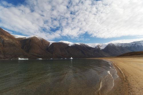 Free Tranquil Arctic shoreline with mountains and clouds, showcasing nature's beauty. Stock Photo