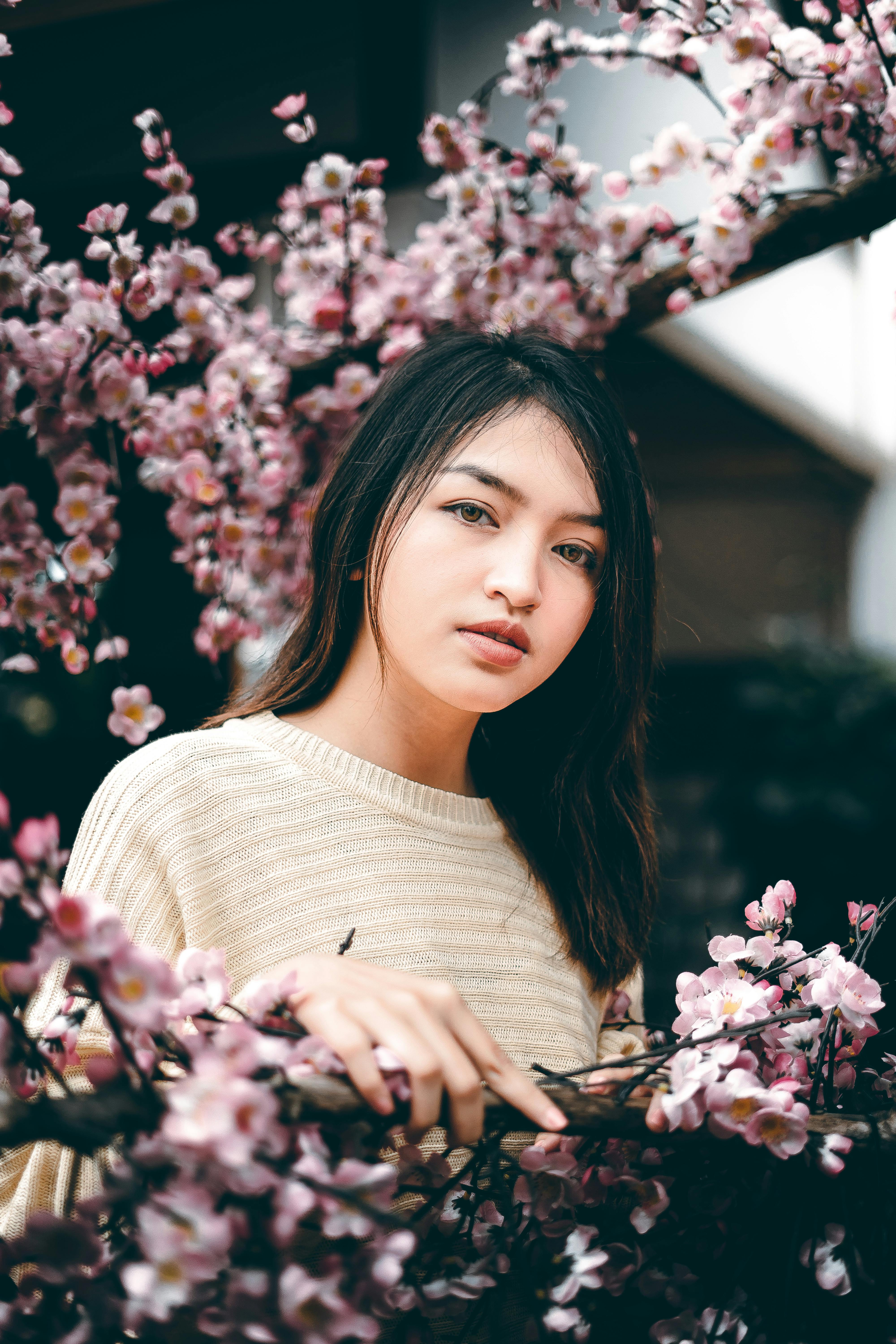 A serene portrait of a young woman surrounded by blooming cherry blossoms outdoors.