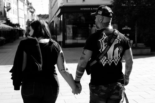Free A couple holds hands while walking on a sunlit city street. Stock Photo