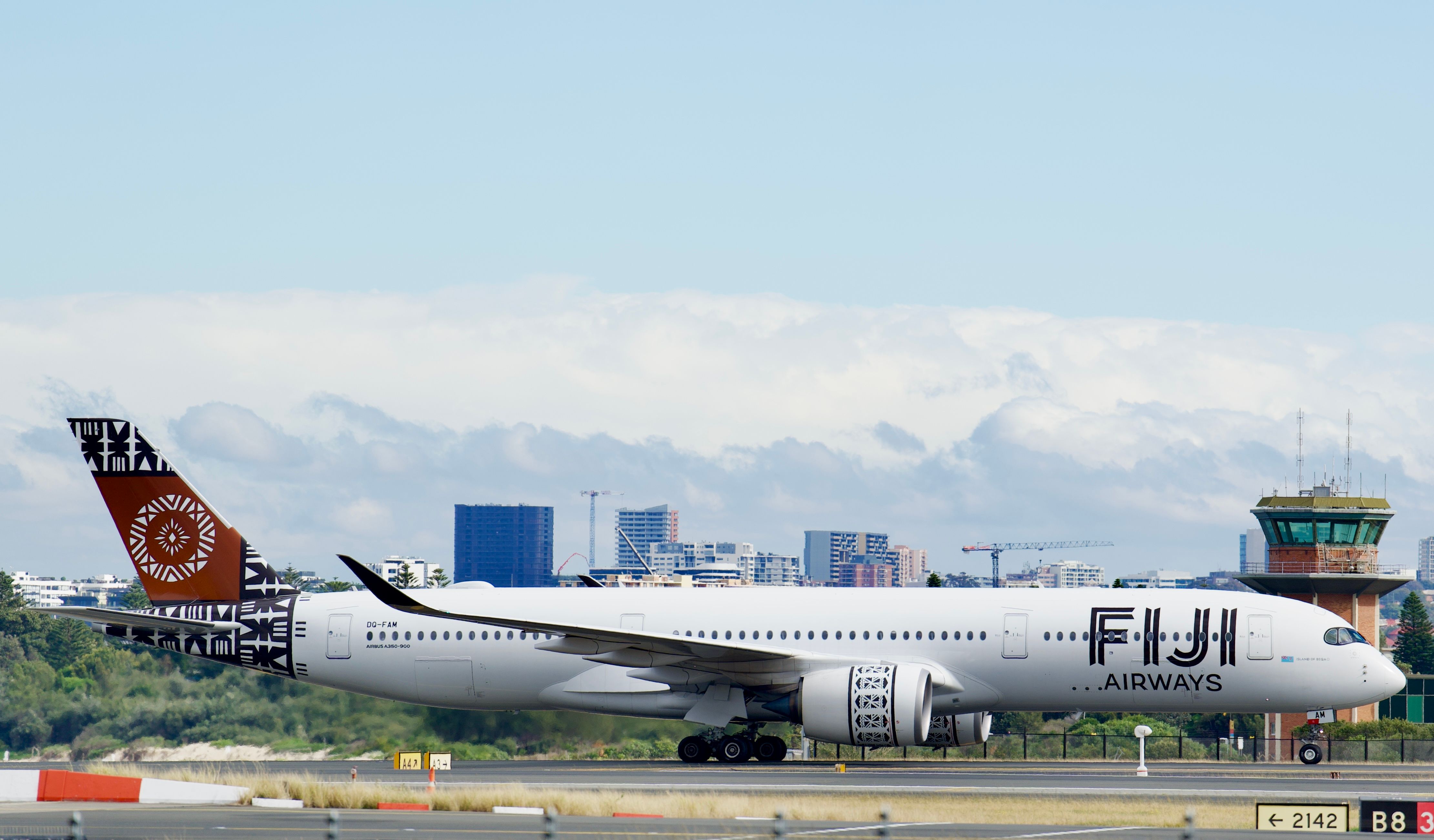 Fiji Airways Airbus A350 taxiing at Sydney Airport with city skyline backdrop.