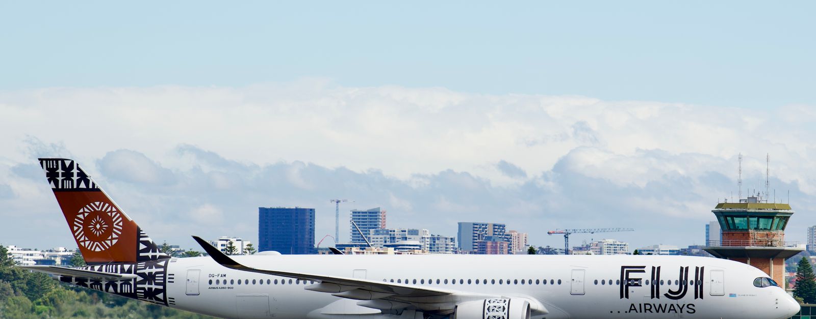 Fiji Airways Airbus A350 taxiing at Sydney Airport with city skyline backdrop.