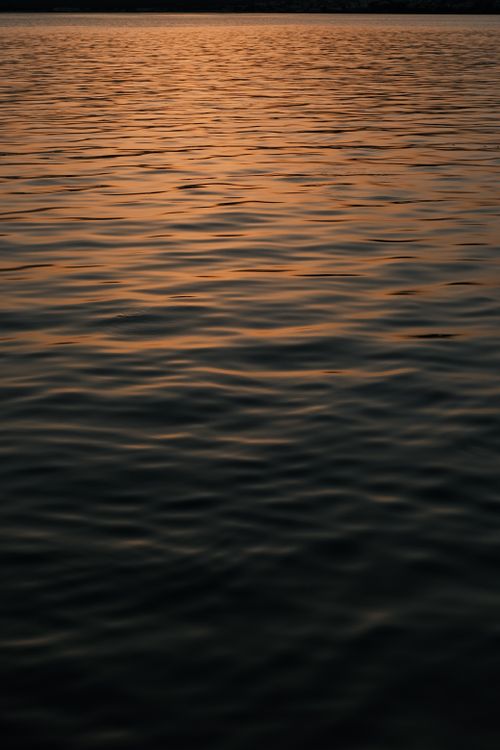 Free A tranquil scene of dark water gently rippling under a warm, sunset glow. Stock Photo